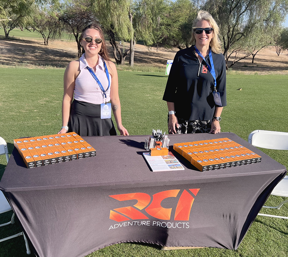 Two RCI sales representatives stand behind a table with several giveaways during a golf outing in Arizona.