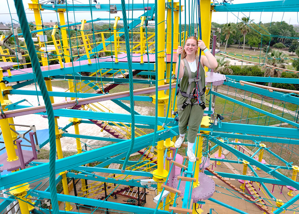 A teenage girl smiles as she walks across a ropes course obstacle at Moody Gardens in Galveston, TX.