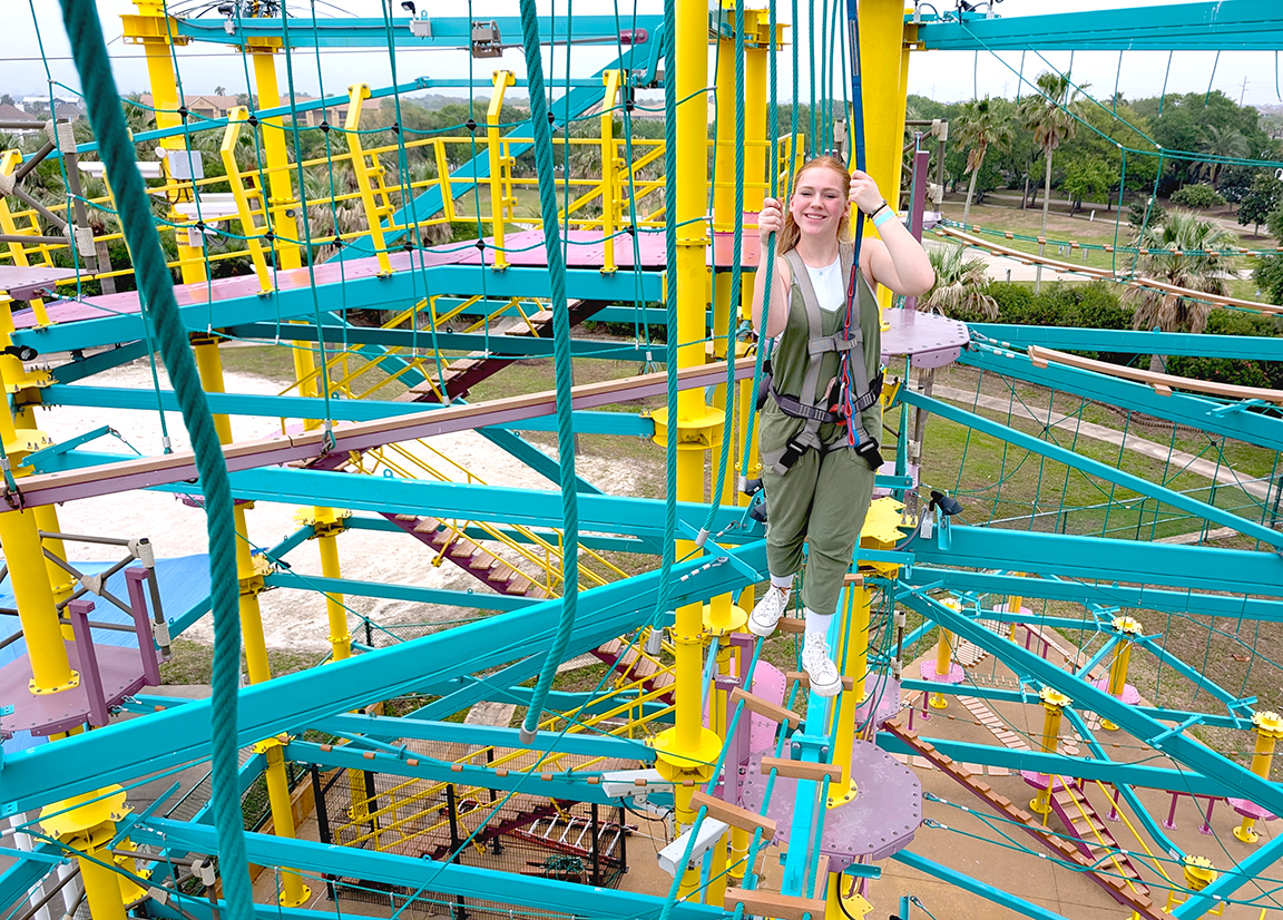 A teenage girl smiles as she walks across a ropes course obstacle at Moody Gardens in Galveston, TX.
